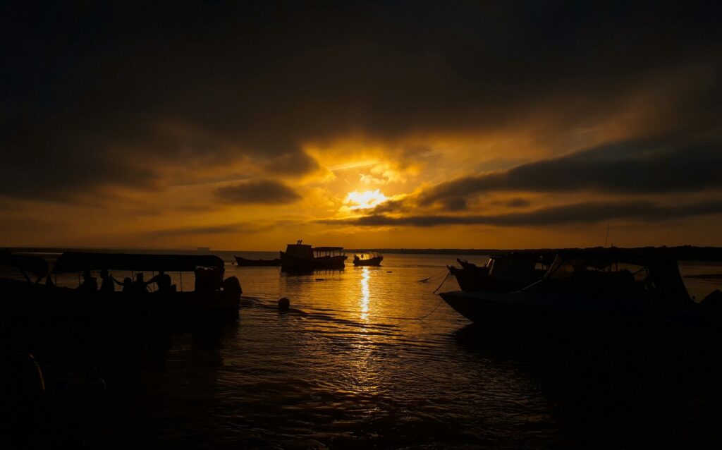 Sunset over a moored boat at Ilha do Mel, by Thay Pellerin