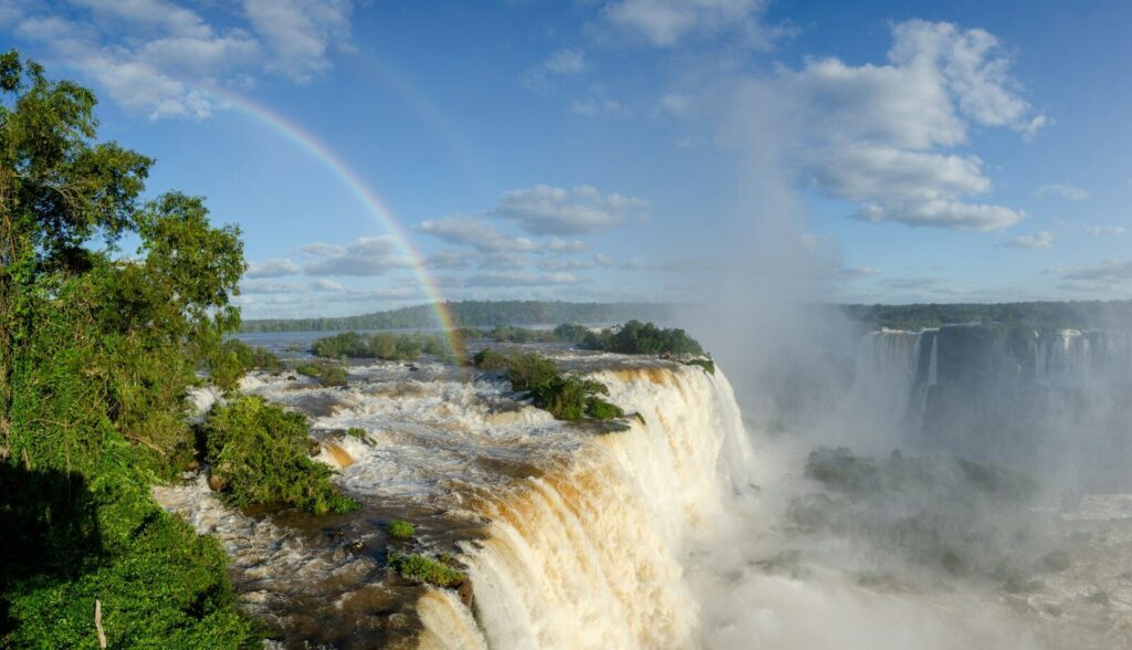 A wide waterfall with a rainbow rising from the spray