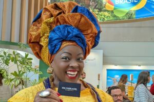 YourBrasil business card held by a woman in traditional Bahian dress at the Brasil pavilion, TTG Travel Experience Rimini 2026